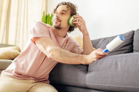 Téléchargez les photos : Handsome man in cozy homewear posing near a couch, holding a sticky roller. - en image libre de droit