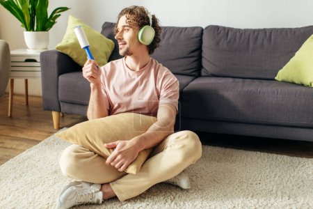 Foto de Un hombre en ropa de casa acogedora sentado en el suelo escuchando música con auriculares. - Imagen libre de derechos