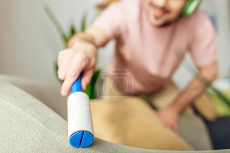 Photo for Handsome man in cozy homewear listens to headphones while cleaning a couch. - Royalty Free Image