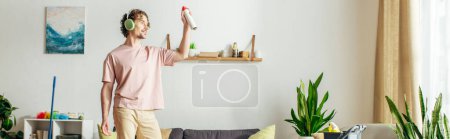 A man in cozy homewear holds a spray in a living room.
