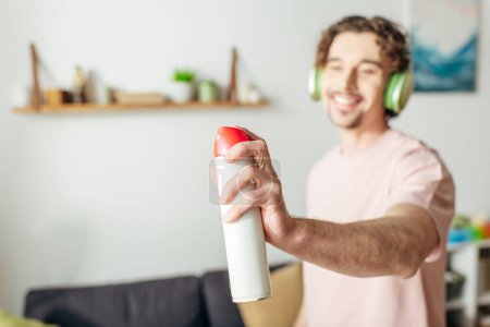Foto de Un hombre en ropa interior acogedora sostiene un aerosol mientras usa auriculares, absorto en la armonía musical. - Imagen libre de derechos