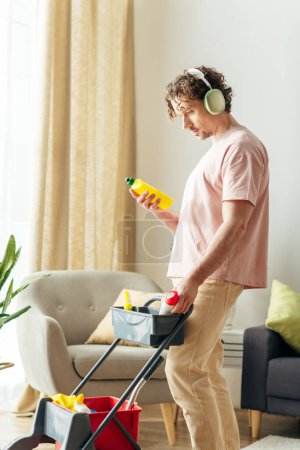 Foto de Un hombre elegante en ropa de casa limpia una acogedora sala de estar con auriculares. - Imagen libre de derechos
