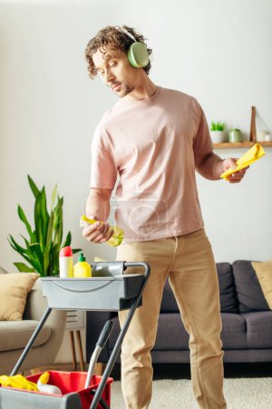 A man in cozy homewear cleans the living room while listening to music through headphones.