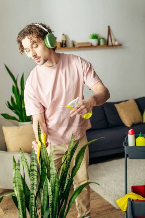 Foto de Un hombre en acogedora ropa de casa se para frente a una planta, con auriculares. - Imagen libre de derechos