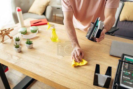 Schöner Mann in kuscheliger Hauskleidung putzt fleißig einen Tisch mit einem Schwamm.