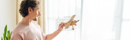 Un hombre en ropa interior acogedora sostiene un avión de juguete en su mano.