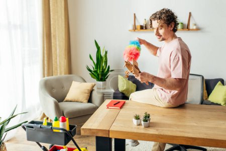 Hombre guapo en ropa de casa acogedora jugando con un juguete mientras limpia en una mesa.