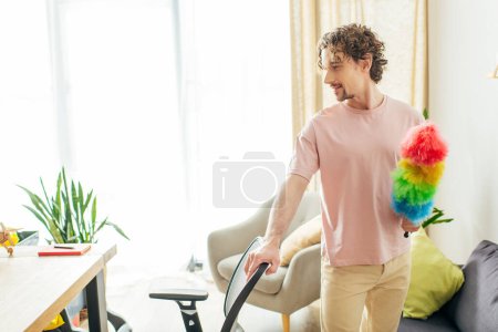 Photo for Handsome man in cozy homewear holding a colorful duster in a living room. - Royalty Free Image