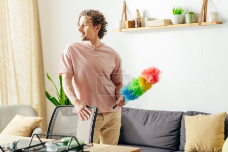Photo for A stylish man cleans the living room with a duster. - Royalty Free Image
