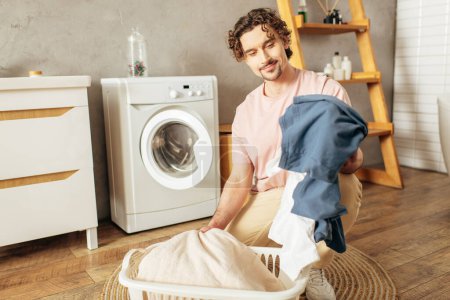 Un hombre en ropa de casa acogedora sostiene una bolsa de lavandería delante de una lavadora.