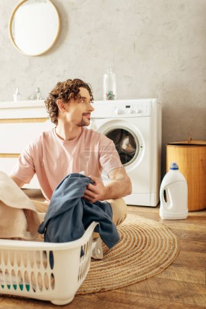 A handsome man in cozy homewear sits beside a laundry basket.