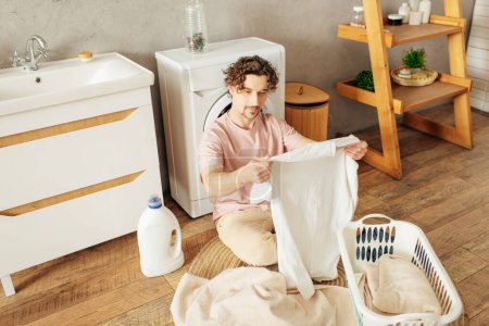 A man in cozy homewear sits on the floor with a laundry basket.
