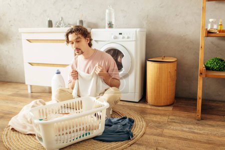 Ein gutaussehender Mann in kuscheliger Homewear sitzt neben einer Waschmaschine.