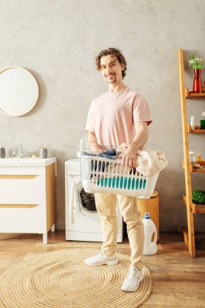 Ein gutaussehender Mann in gemütlicher Hauskleidung hält einen Wäschekorb in einem Raum.