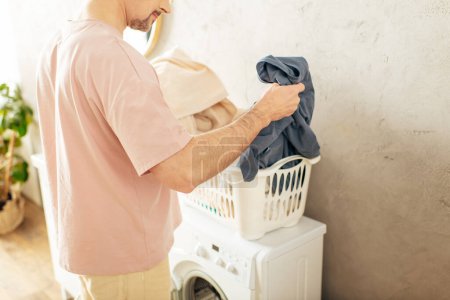 Un hombre guapo en ropa de casa acogedora está al lado de una lavadora.