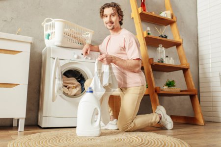 A handsome man in a pink shirt meticulously doing laundry at home.