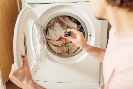 Un hombre guapo en ropa de casa acogedora poner detergente a la ropa en una lavadora.
