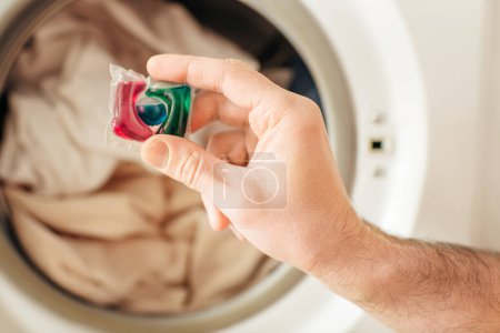 Foto de A hand holding a detergent in front of a washing machine. - Imagen libre de derechos