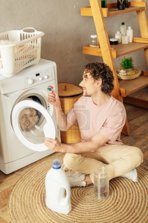 A man in cozy homewear sits next to a washing machine.