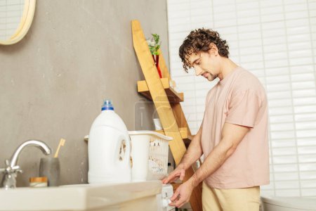 Foto de Un hombre guapo en ropa de casa acogedora lavando su ropa. - Imagen libre de derechos