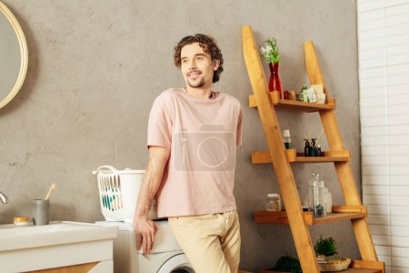 Foto de Hombre guapo en ropa de casa acogedora de pie junto a una lavadora en un baño. - Imagen libre de derechos