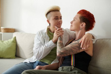 Téléchargez les photos : Deux femmes tatouées s'assoient étroitement ensemble sur un canapé, exposant leur art corporel unique dans un cadre intérieur confortable. - en image libre de droit