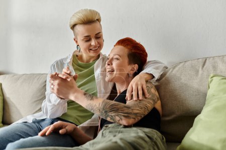 Photo for Two women, a lesbian couple, with short hair and tattoos, relax together on a couch. - Royalty Free Image