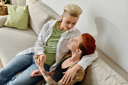 Téléchargez les photos : Deux femmes, un couple de lesbiennes aux cheveux courts, assis ensemble sur un canapé confortable à la maison, partageant un moment intime. - en image libre de droit