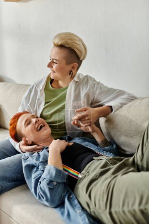 Foto de Una pareja de lesbianas con el pelo corto sentados juntos en un sofá, compartiendo un momento de risa y alegría. - Imagen libre de derechos