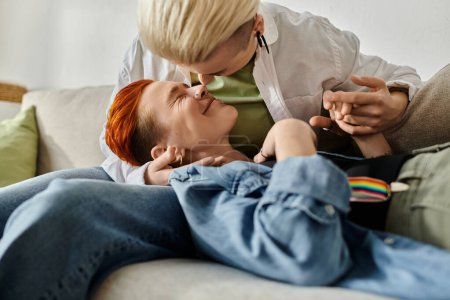 Téléchargez les photos : Un couple de lesbiennes aux cheveux courts s'embrassant affectueusement sur un canapé confortable à la maison. - en image libre de droit
