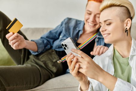 Foto de Dos mujeres con el pelo corto, una pareja lesbiana, sentadas en un sofá, sosteniendo una tarjeta de crédito, discutiendo asuntos financieros. - Imagen libre de derechos