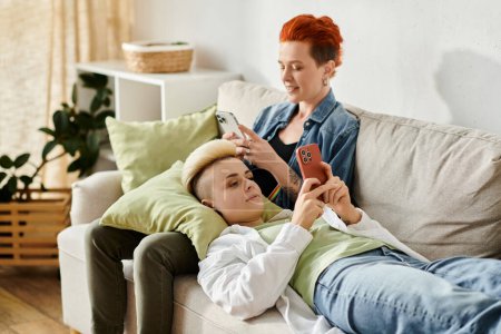 women with short hair sit on a couch, engrossed in their cell phones.