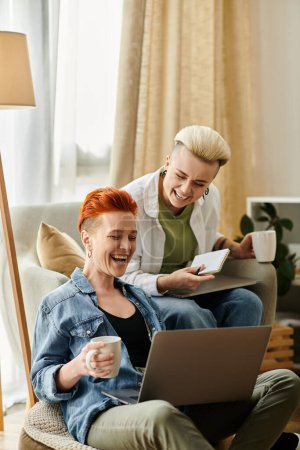 Téléchargez les photos : Deux femmes aux cheveux courts s'assoient sur un canapé, absorbées par un écran d'ordinateur portable, partageant un moment de connexion. - en image libre de droit