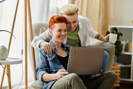 Photo for Two women, a lesbian couple, sit on a couch, engrossed in a laptop screen, sharing a quiet moment of togetherness. - Royalty Free Image