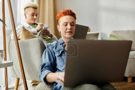 Téléchargez les photos : Deux femmes avec les cheveux courts assis sur un canapé, absorbés dans un ordinateur portable ensemble à la maison. - en image libre de droit