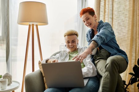 Téléchargez les photos : Un couple lesbien aux cheveux courts assis sur un canapé, concentré sur l'utilisation d'un ordinateur portable ensemble à la maison. - en image libre de droit