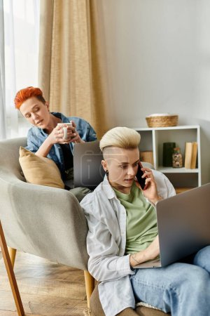 Dos jóvenes sentados de cerca en un sofá, enfocados en sus computadoras portátiles, absortos en sus tareas individuales.