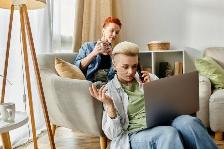 Una pareja lesbiana en un sofá usando un portátil y hablando por teléfono.