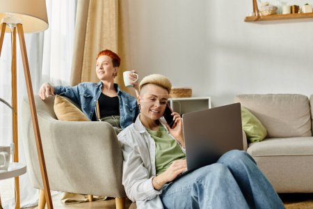 Téléchargez les photos : Un couple de lesbiennes se détend sur un canapé, sirotant du café et utilisant un ordinateur portable ensemble. - en image libre de droit