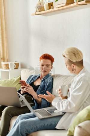 Photo for Two women with short hair sit on a couch, engrossed in conversation on their laptops. - Royalty Free Image