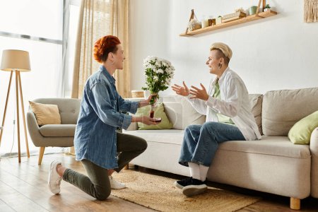 Eine Frau überreicht ihrem Partner, der zu Hause auf einer Couch sitzt, Blumen und macht ihm einen Heiratsantrag