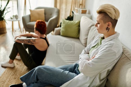A lesbian couple with short hair sitting separately on a cozy couch in a stylish living room.