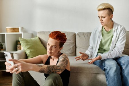 Photo for Two women with short hair engaged in conversation about online cheating while sitting on a sofa in a living room. - Royalty Free Image
