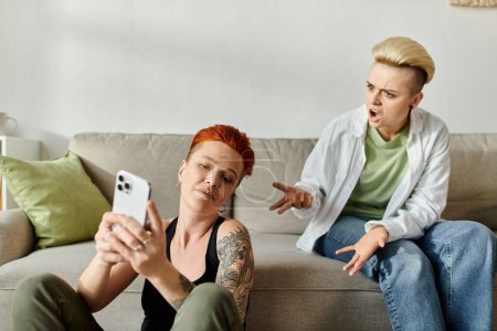 Dos mujeres lgbt sentadas en un sofá, dedicadas a navegar juntos por un teléfono celular.