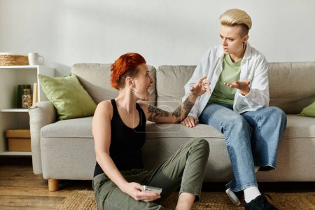 Dos mujeres con el pelo corto se sientan en un sofá, absorto en la conversación emocional