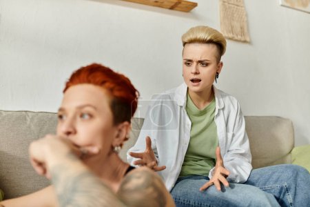 Deux femmes aux cheveux courts assises sur un canapé, engagées dans une conversation émotionnelle à la maison.