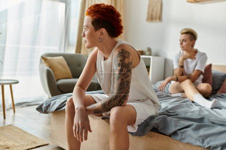 Ein lesbisches Paar mit kurzen Haaren sitzt auf einem Bett und hat einen Konflikt