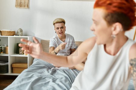 Zwei Frauen, ein lesbisches Paar mit kurzen Haaren, sitzen auf einem Bett und unterhalten sich wütend im Schlafzimmer.