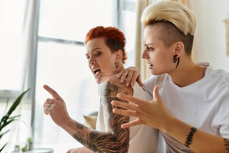 Dos mujeres con tatuajes se involucran en una discusión acalorada en una elegante sala de estar. Cabello corto, estilo de vida LGBT evidente.
