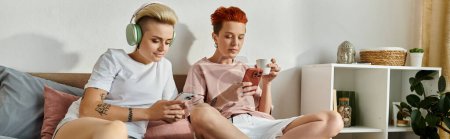 Foto de Dos jóvenes sentados en una cama, absortos en jugar juegos de teléfonos inteligentes juntos. - Imagen libre de derechos